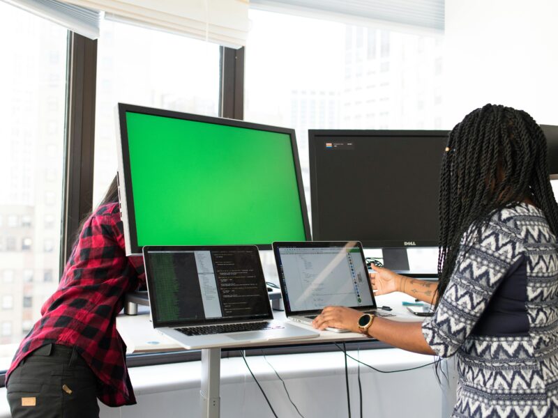 Fotografía donde se ve a una mujer trabajando en una mesa con varias pantallas de ordenador